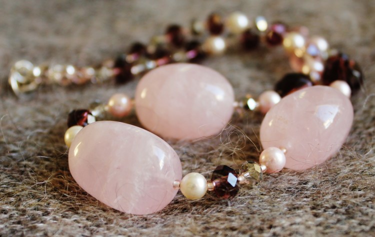 Kaulakorussa suuria ruusukvartsihelmiä, Swarovskin huurrekristallihelmiä, sekä erilaisia lasihelmiä. Tässä yksilössä lukko Israel Pewter-metalliseoksesta.