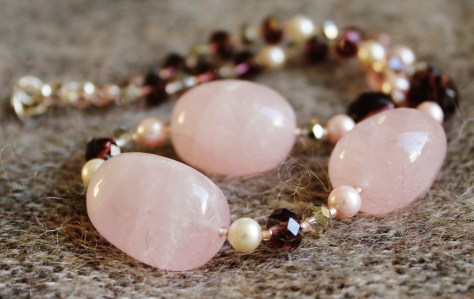 Kaulakorussa suuria ruusukvartsihelmiä, Swarovskin huurrekristallihelmiä, sekä erilaisia lasihelmiä. Tässä yksilössä lukko Israel Pewter-metalliseoksesta.